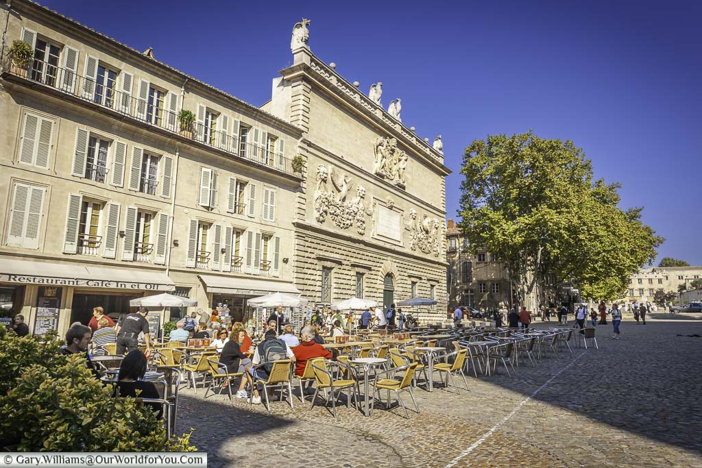 A cobbled street scene in Avignon, France, with tables and chairs lined up outside a cafe