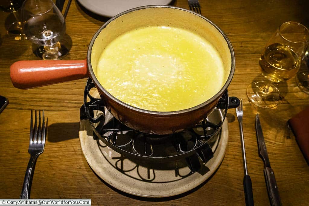 A bubbling pot of cheese fondue served in a cast-iron saucepan over a low heat.