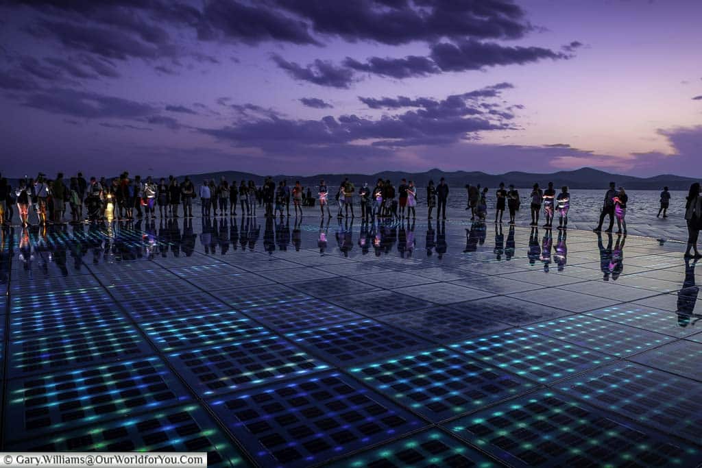 People gather around the ‘Greeting to the Sun’ light display at Zadar’s Riva at dusk. They are illuminated by the LED floor tiles that make up this open-air art installation.