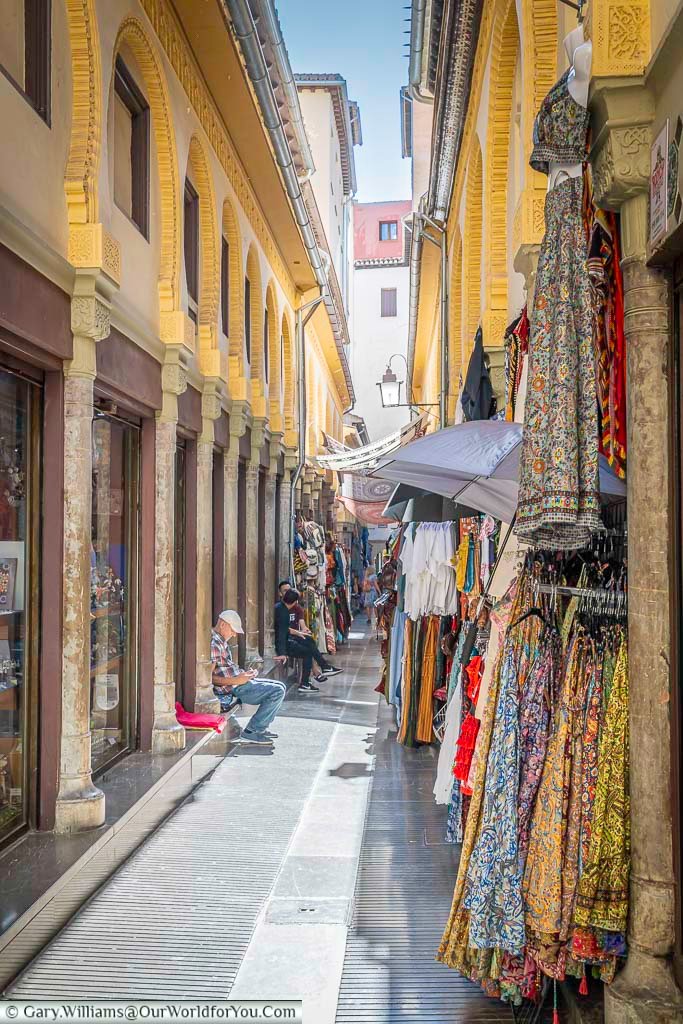 a narrow lane lined with shops selling local scarves, dress and other clothes in old granada in andulucia, spain