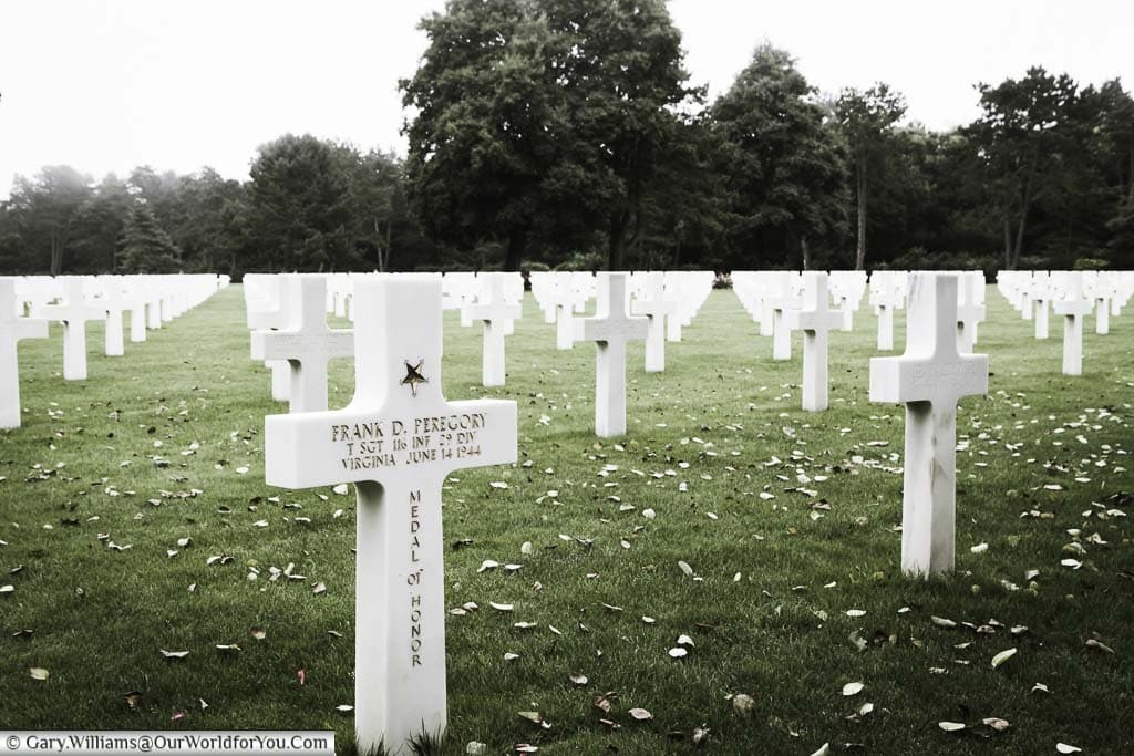 A field of headstones in the Normandy American Cemetery. The cross of Frank D Peregory is decorated with a gold star and Medal of Honor inscription.