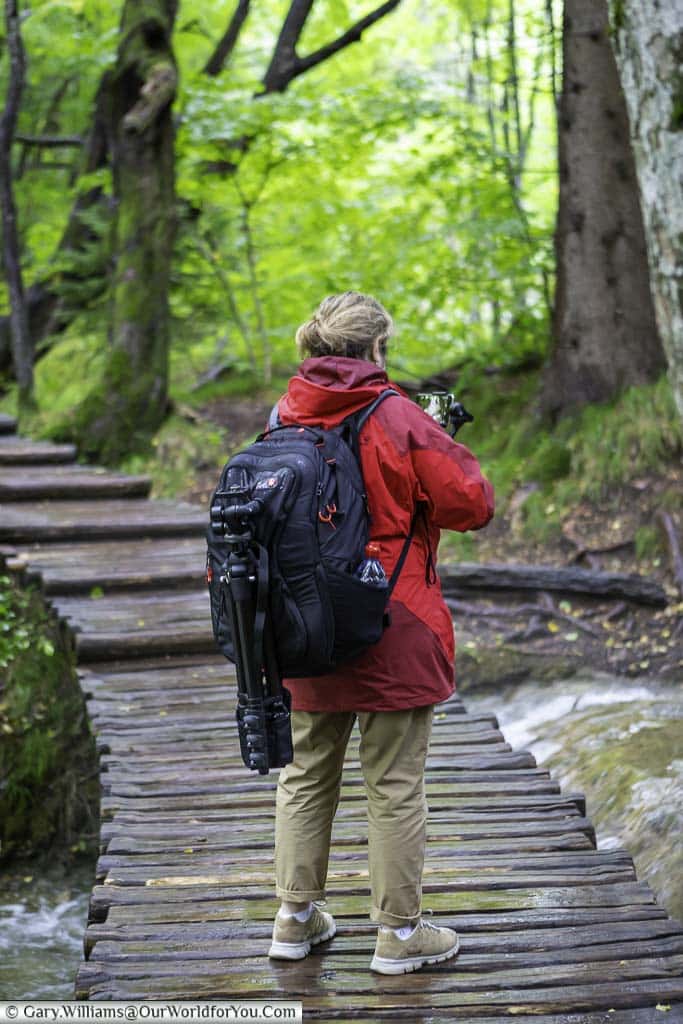 a view of the back of janis in her red jack wolfskin jacket on a wooden path videoing a waterfall in plitvice lakes, croatia