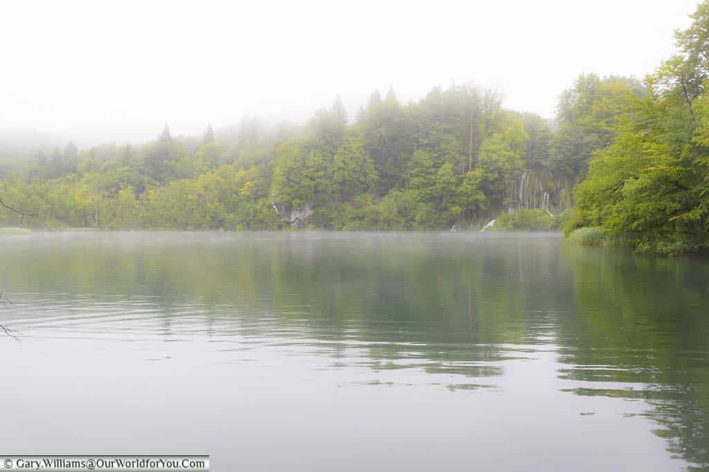 a bright misty view over the upper lakes of plitvice in croatia against a backdrop of lush green trees