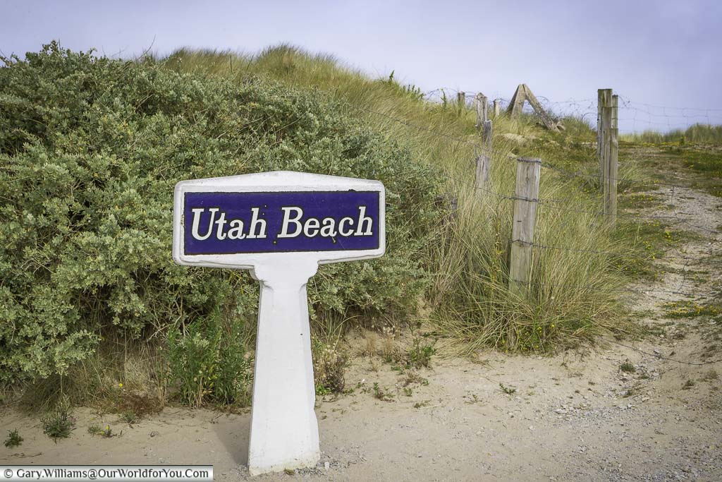 The white concrete sign for Utah beach in front of a path that leads to the Normandy shoreline