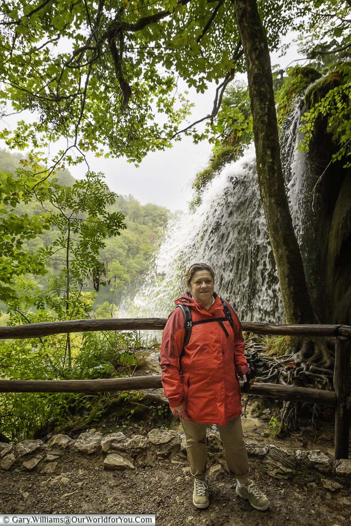 Janis standing in front of a rustic wooden fence in front of a waterfall in the plitvice lakes national park in croatia