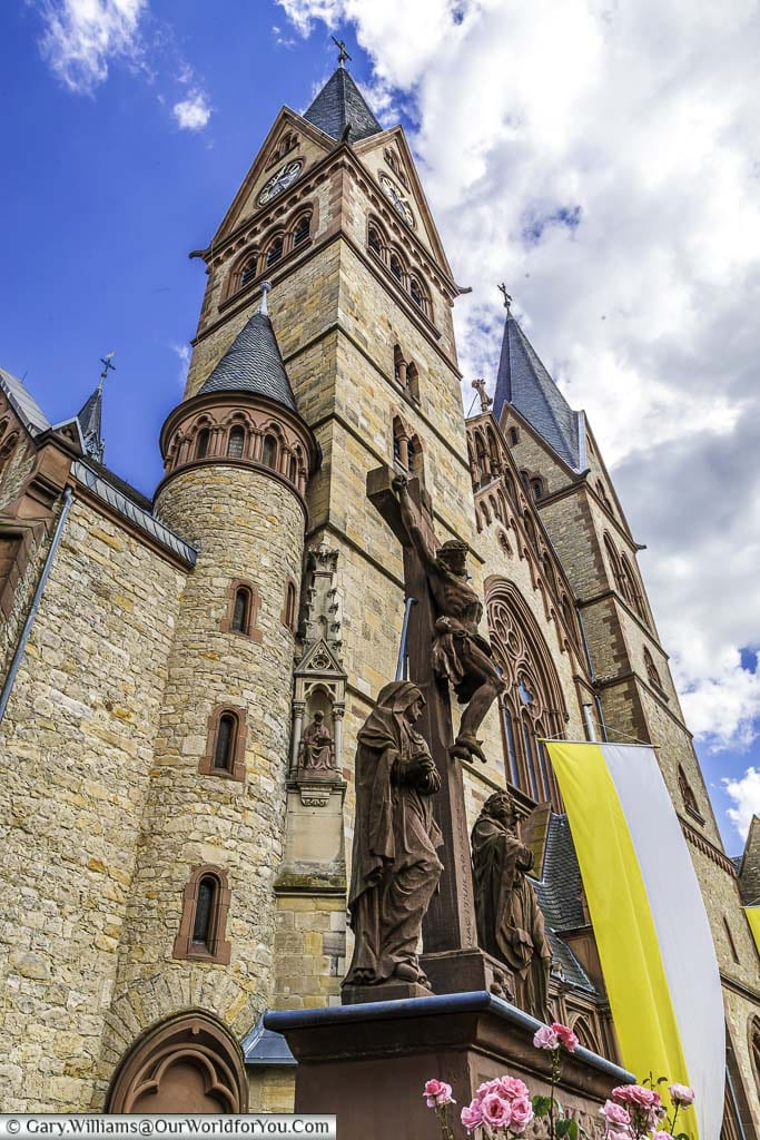 A portrait, wide angle view of a statue of Christ on the cross in front of the twin towers of the Cathedral of Bergstraße in Heppenheim.