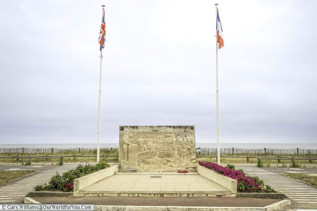 A memorial on Sword beach in Normandy. The stone monument flanked by two flag poles, the Union flag atop one, the French Tricolour the other.