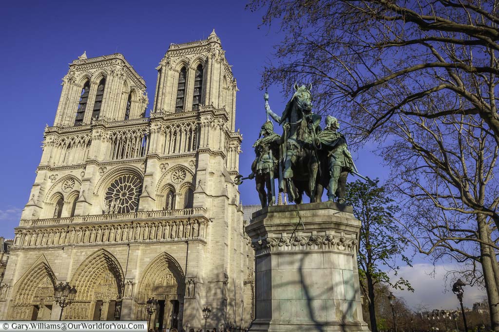 A statue to Charlemagne and his knights in front of the Cathédrale Notre-Dame de Paris reflected in early spring light under deep blue skies
