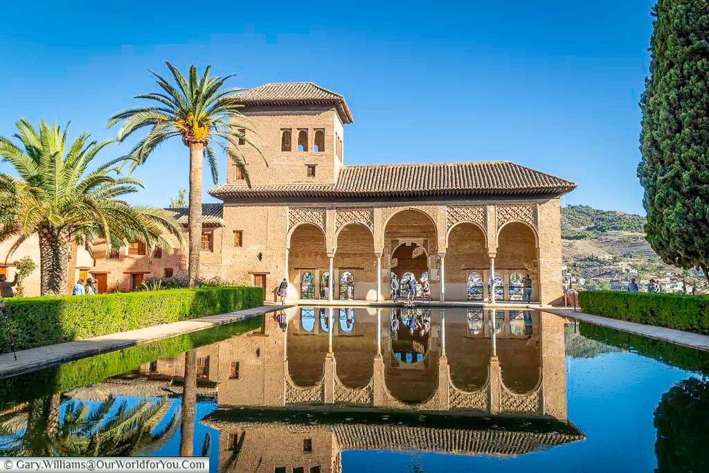 the partal palace pavilion reflected in a huge pond in front of it under deep blue skies at the alhambra palace in granada, spain