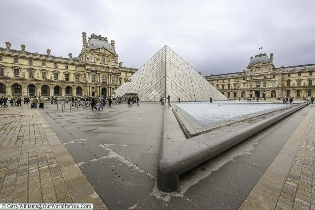 The courtyard of the louvre art gallery and museum in paris with its now iconic glass pyramid in the centre.