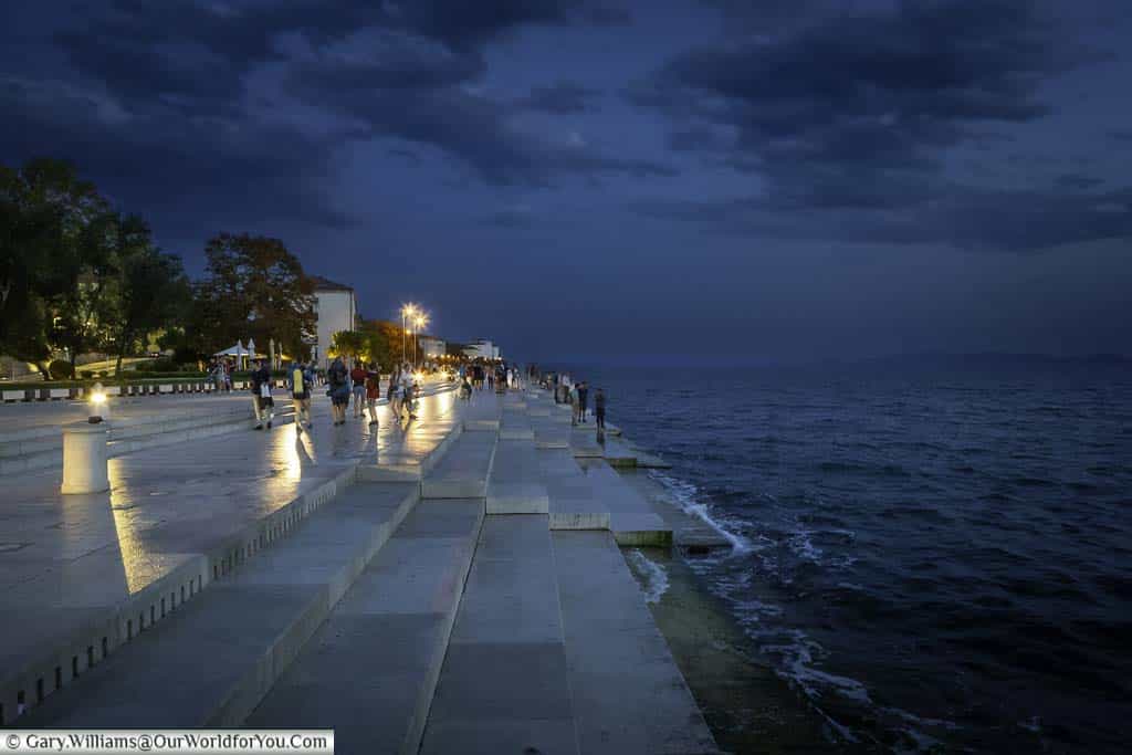 The Sea Organ, hidden under Zadar’s Riva at dusk, after the sun has set, but there is still blue light. Shallow steps lead down to the waters of the Adriatic Sea lapping against the edge.