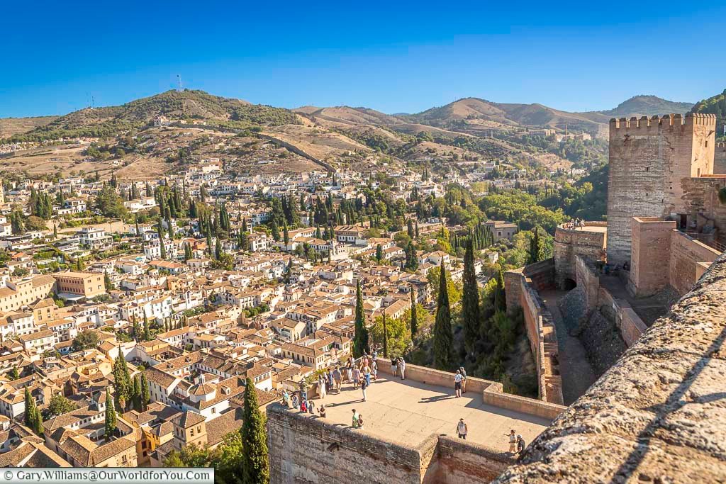 the views from the tower of homage in the alcazaba at the alhambra palace, across the rooftops of granada to the mountains beyond