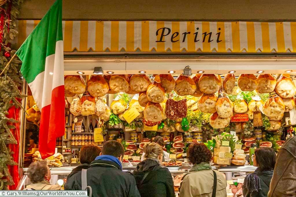 The Perini stall inside the Mercato Centrale in Florence, Italy. Cured hams hang from the counter as people queue.