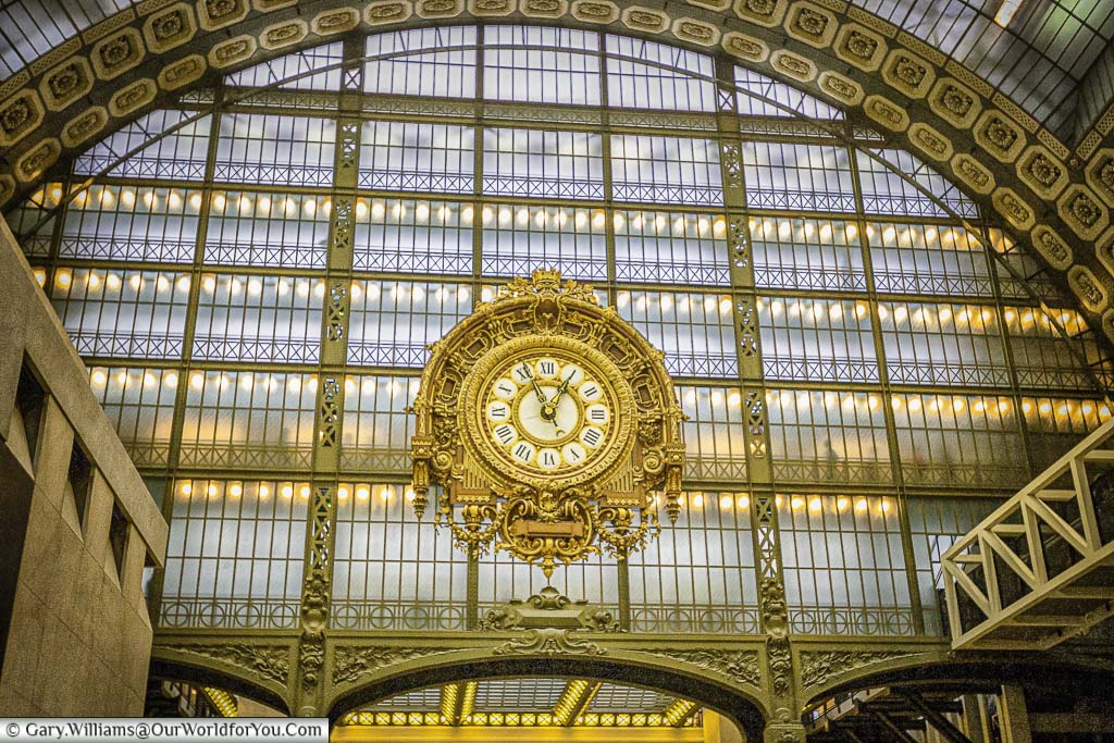 The ornate gilded clock inside the Museum D'Orsay against the backdrop of the glass and iron lattice framework, a throwback to when the building was a railway station.