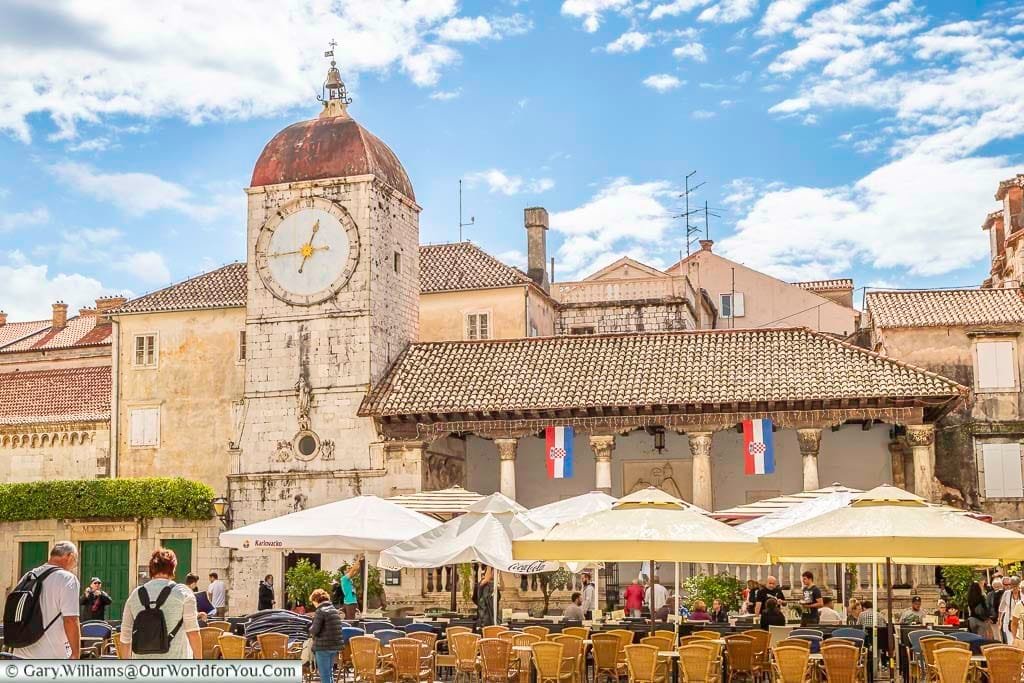 canopies over tables and chairs, in front of a historic clock tower in the loggia di trogir, in the centre of old trogir, croatia