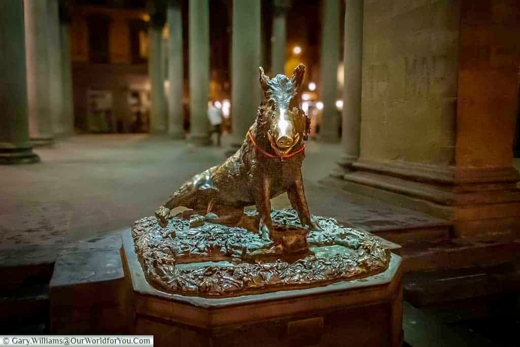 A bronze statue of a wild boar in a seated postition at the edge of a market square in Florence. Its snout buffed by the number of people that have touched it for luck.