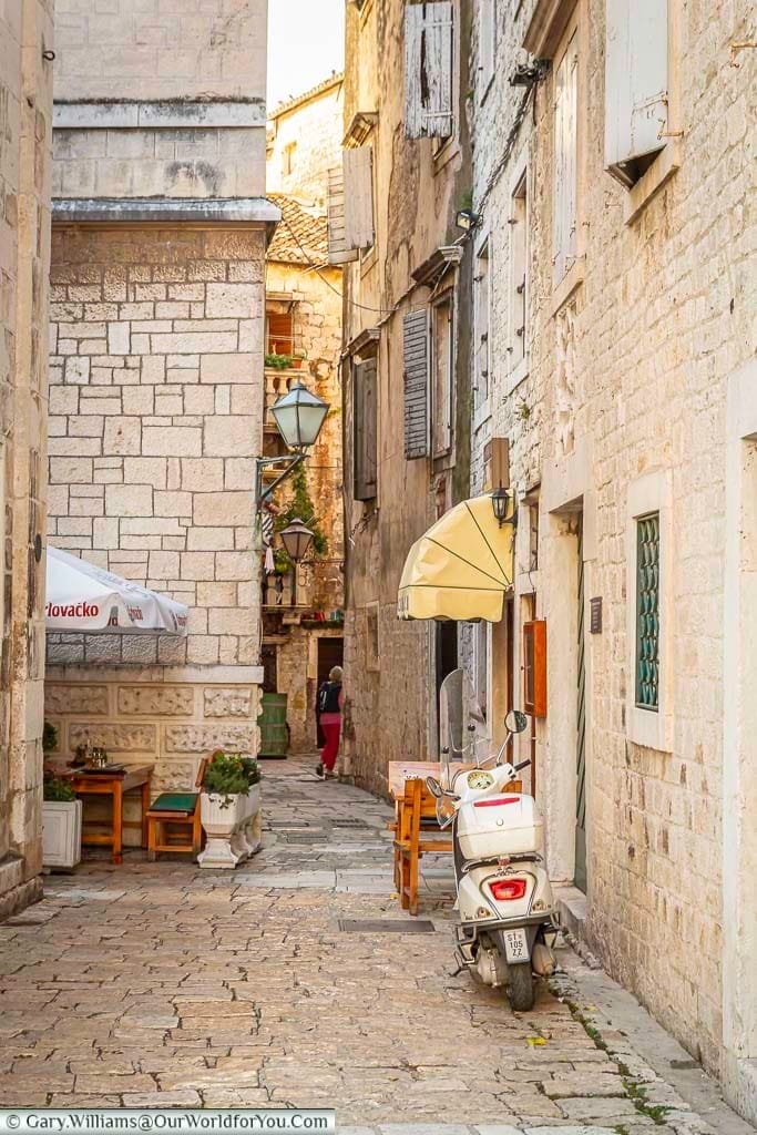 a cream moped parked outside a home in the cobbled lanes of historic old trogir, croatia