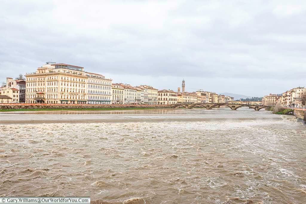 The murky waters of the arno river as it runs through florence, italy, with the city in the background.