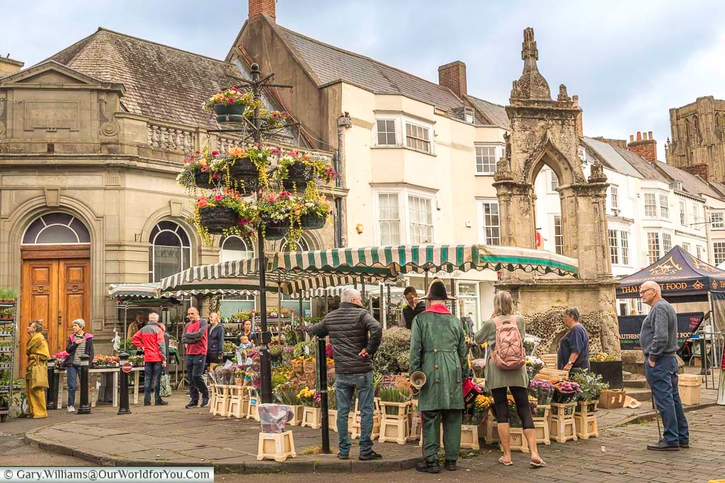 Wells town cryer at the flower stall in front of the wells market cross on the wednesday market