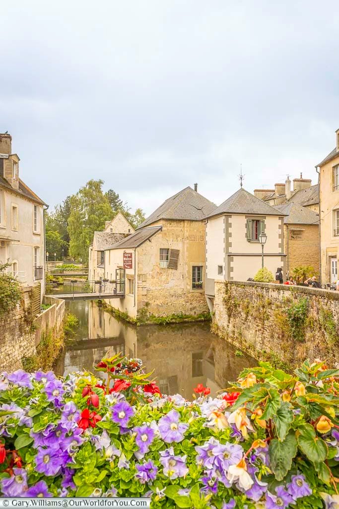 the flower-lined view from the pont saint-jean in bayeux along the river aure with medieval buildings lining the route