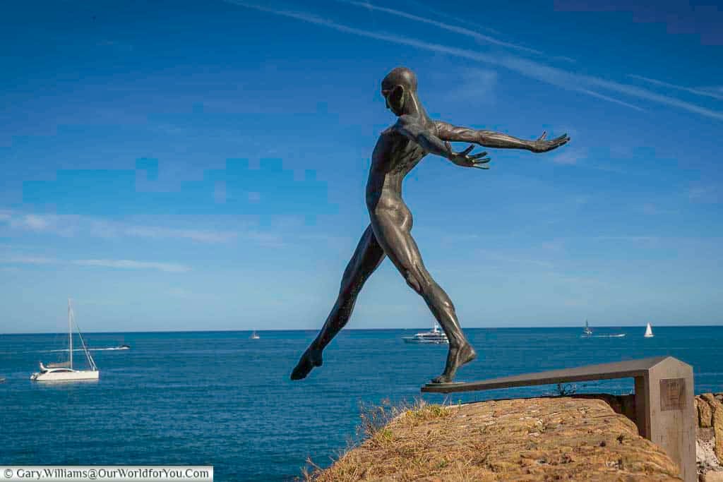 A bronze statue of a naked male figure about to launch off a diving board into the mediterranean sea at antibes in from of small sailing boats