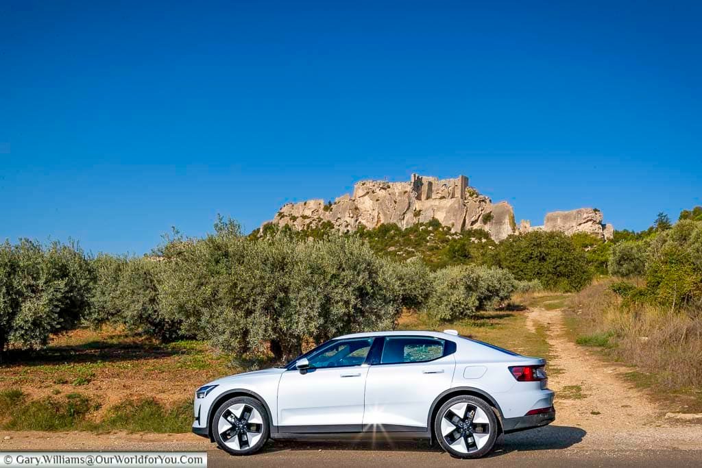 Our Polestar 2 EV is parked on the roadside, with the hillside village of Les Baux-de-Provence in the background.