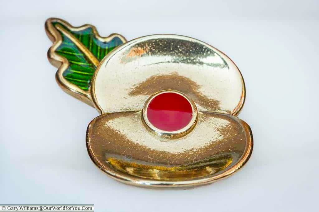 A close-up of the brass royal british legion passchendaele poppy pin, with a red enamel centre and a green leaf