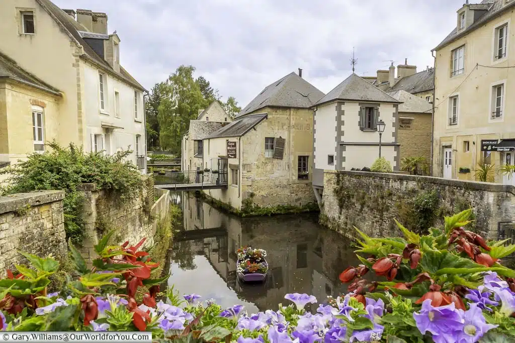 The flower-lined view from the pont saint-jean in bayeux with planted out rowing boat in the river aure and medieval buildings lining the route