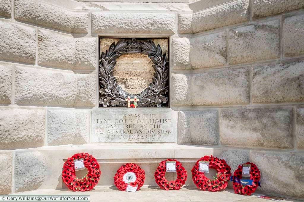 Five poppy wreaths at the base of the cross of sacrifice below a plaque to the 3rd australian division who captured the blockhouse at tyne cot, belgium