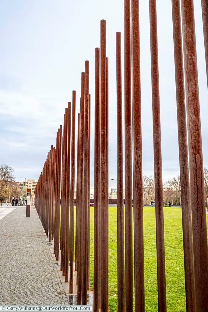 A section of the Berlin Wall where the structure has been replaced with evenly spaced iron rods that allow you to see through where the wall once stood.
