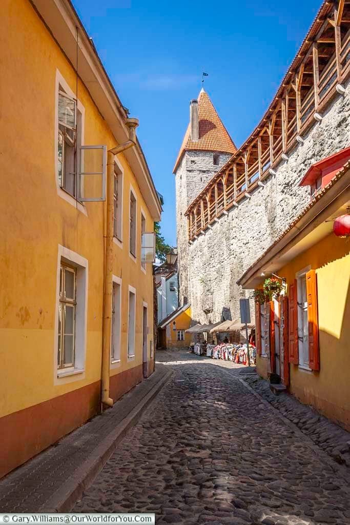 A cobbled lane, lined will stalls, inside the old city walls of tallinn, estonia, with a watchtower in the distance