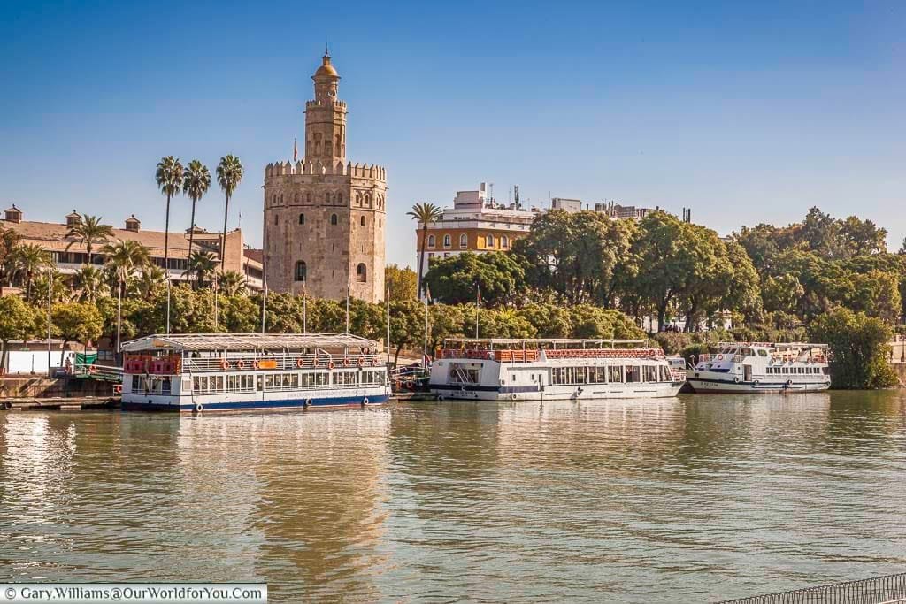Tourist pleasure boats line the edges of the Guadalquivir river in front of the Moorish Torre del Oro.