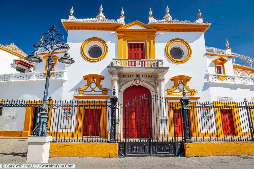 The traditional main entrance to Plaza de Toros, or bullring. The doors are painted a deep red against a white building with Ocre coloured details.