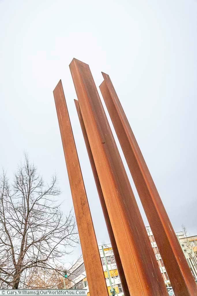 Four rusting iron girders pointing towards the sky representing of the Watchtower Memorial Strelitzer Strasse.