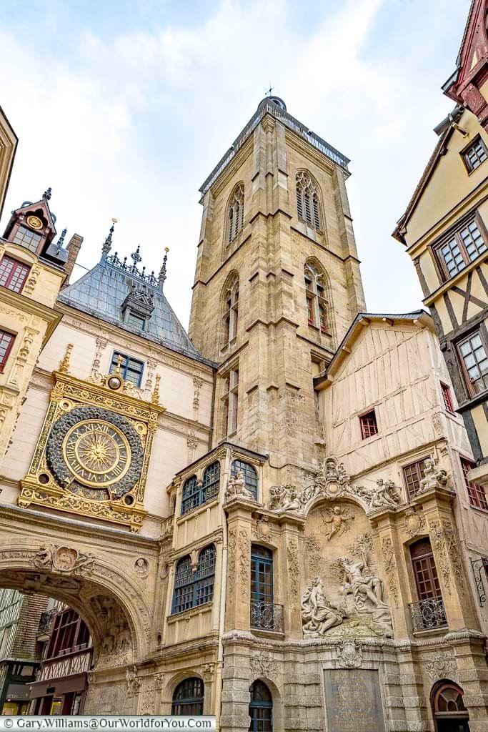 Rouens famous Gros-Horloge. An ornate, gold-trimmed, clock mounted above an arch in one of the old town's thoroughfares next to a stone belfry.
