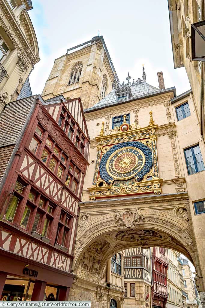 Looking through the arch under Rouens famous Gros-Horloge. An ornate, gold-trimmed, clock mounted on one of the old town's thoroughfares next to a stone belfry.