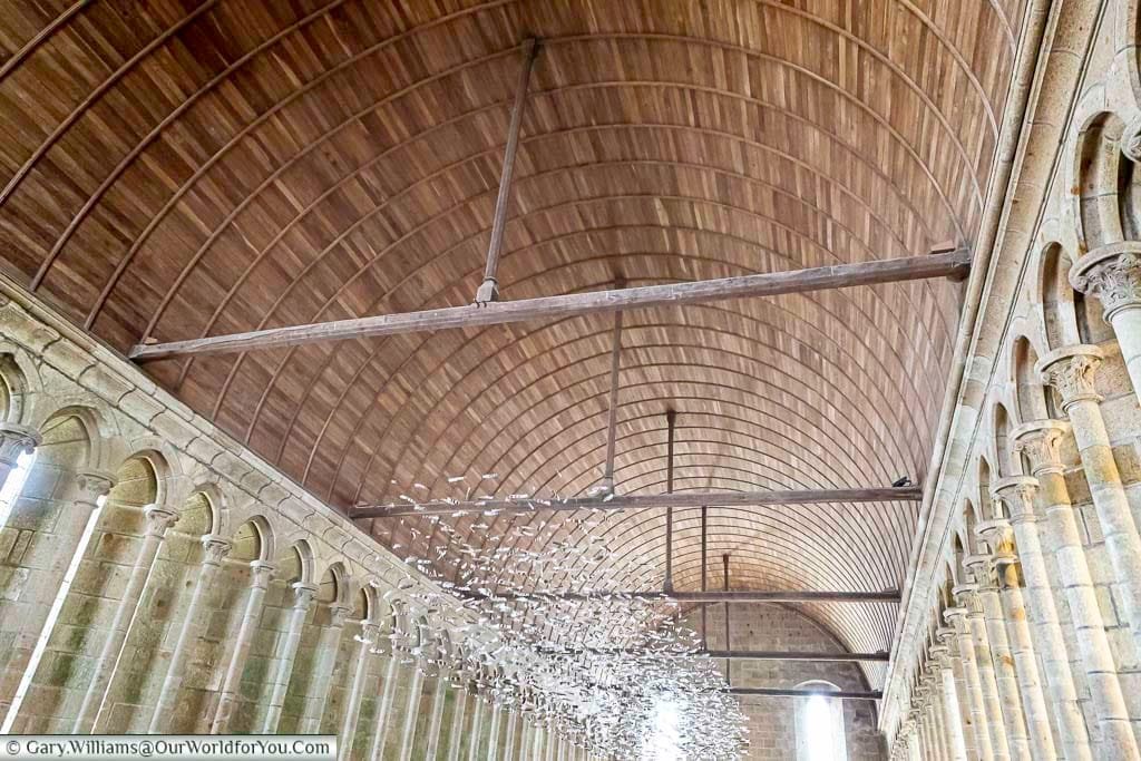 The roof of the refectory inside the Abbey of Mont-Saint-Michel. The roof is lined with wood and is supported on either side by stone columns.