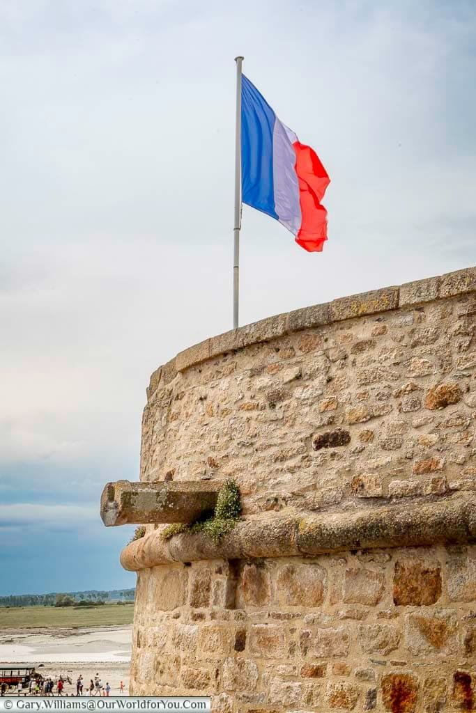 The French Tricolor flag flying high over the ramparts of Mont-Saint-Michel Abbey.