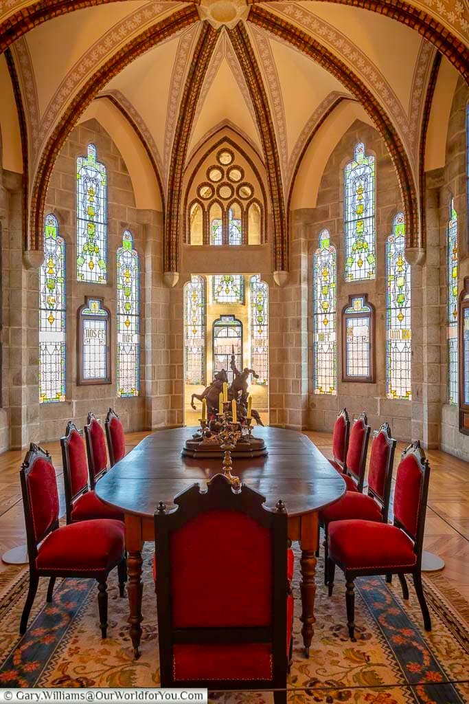 Ten red velvet chairs around an oval table in the dining room, with its stained glass windows, of the episcopal palace of astorga in northern spain