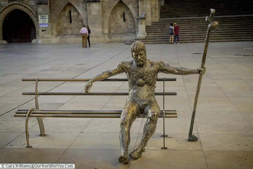 A close-up of a brass figure representing a pilgrim sitting on a bench in burgos in front of the cathedral