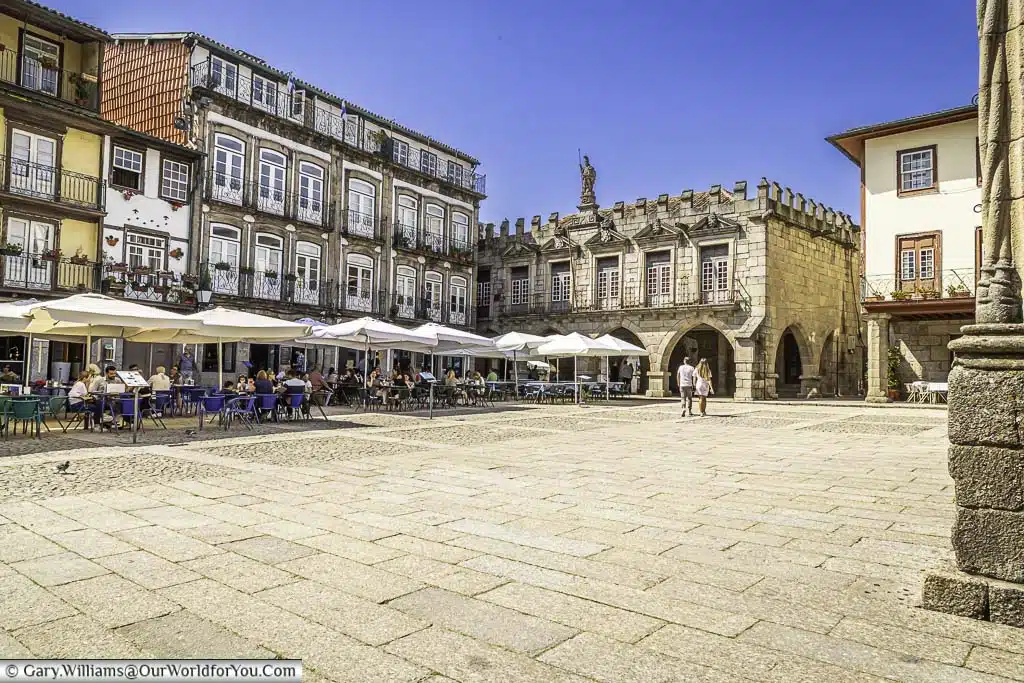 The Largo da Oliveira square in Guimarães, Portugal, where diners sit at restaurants lining the square, and others walk through the historical old town.