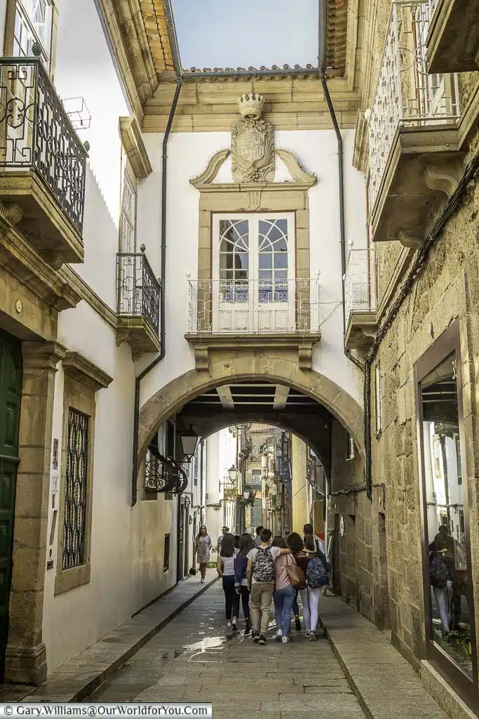 A group of young people walking under an arch connecting buildings on the rua de santa maria in guimarães, portugal