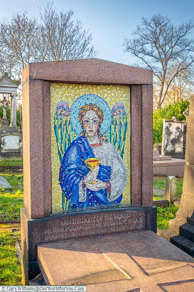 The image features a distinctive grave marker in West Norwood Cemetery, London, adorned with a vibrant mosaic depicting a winged angel holding a chalice. Below the mosaic, an inscription reads "I AM THE LIGHT OF THE WORLD HE THAT FOLLOWETH ME SHALL NOT WALK IN DARKNESS BUT SHALL HAVE THE LIGHT OF LIFE."
