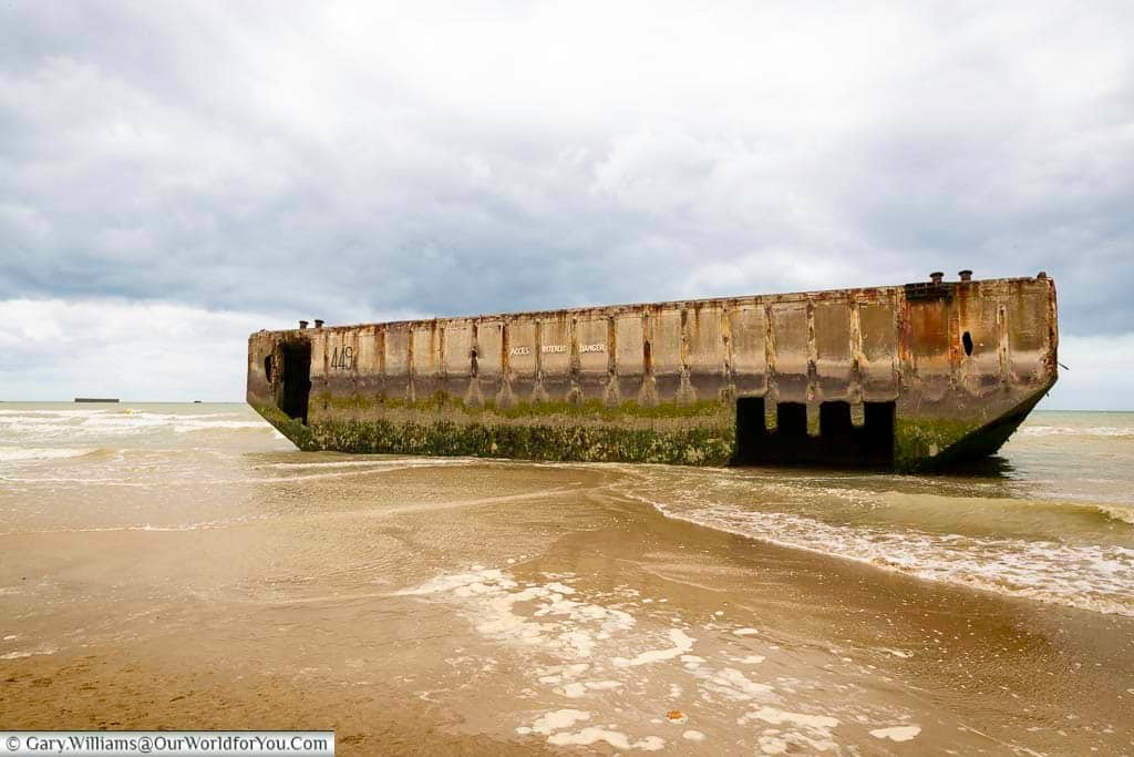 The image shows a section of the Mulberry B artificial harbour, a large, weathered concrete structure partially submerged in the water off the coast of Arromanches. This remnant of the D-Day landings serves as a powerful reminder of the Allied efforts during World War II.
