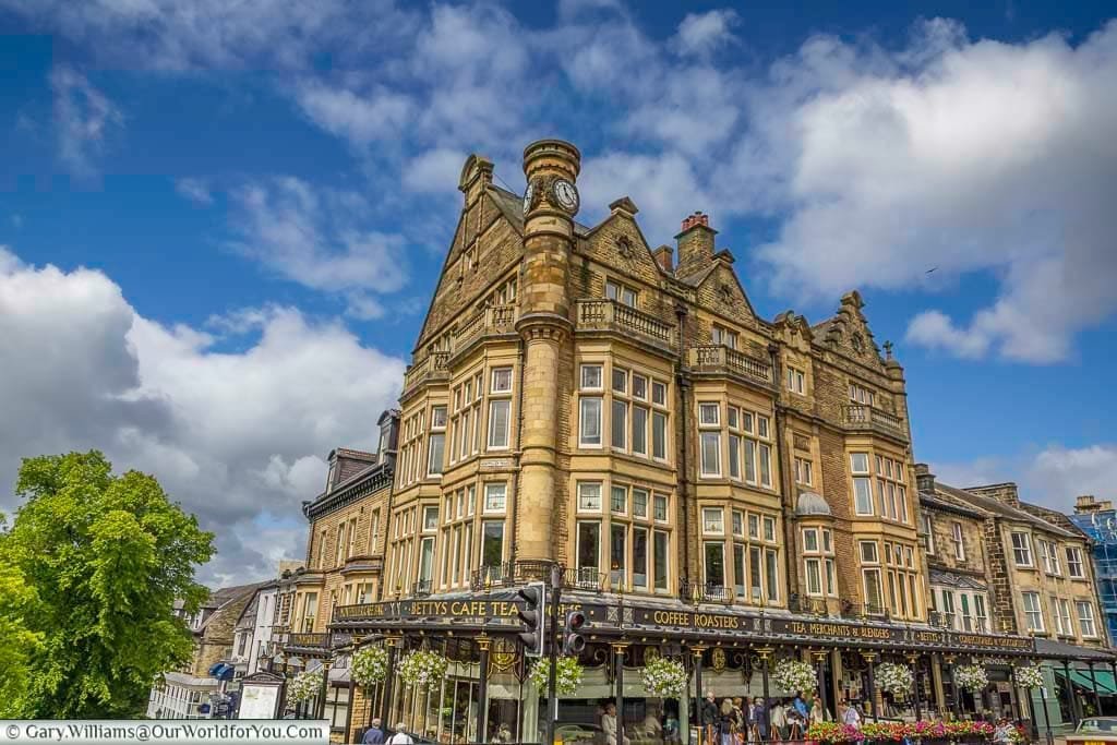 A grand corner view of Bettys Café Tea Rooms in Harrogate, Yorkshire, housed in an elegant Edwardian building adorned with floral displays and traditional signage. This iconic destination blends timeless charm with world-renowned tea and pastries, making it a must-visit spot for anyone exploring Yorkshire.