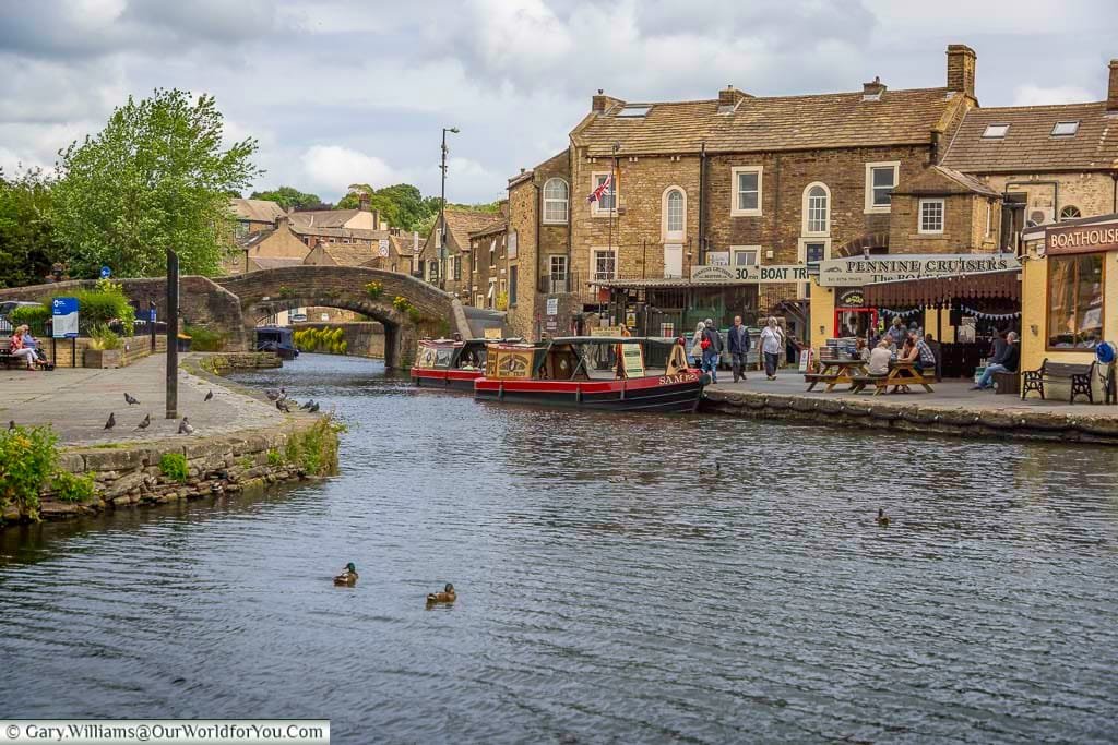 A picturesque view of the canalside in Skipton, Yorkshire, featuring charming narrowboats, a stone footbridge, and bustling local shops and cafés. This scenic market town along the Leeds and Liverpool Canal is a must-visit destination for visitors exploring Yorkshire’s heritage and waterways.