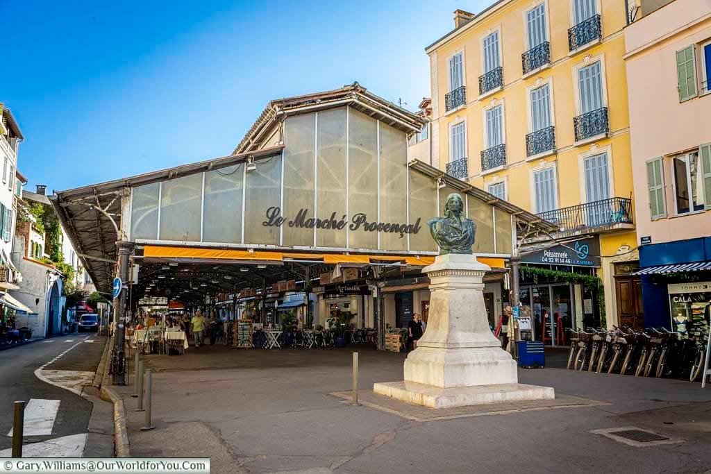 The entrance to Le Marché Provençal in Antibes, France, features a lively square with a prominent statue, surrounded by charming historic buildings. This popular market hub offers fresh produce and local goods in a vibrant setting that reflects the town’s Mediterranean character.