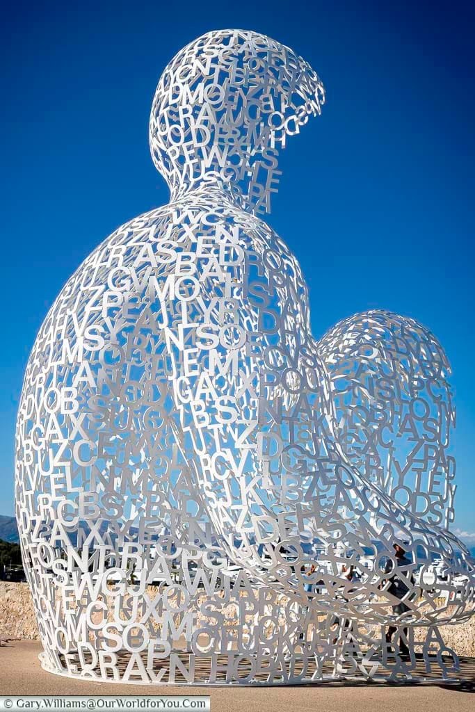A monumental white sculpture made of interlocking letters forms the silhouette of a seated human figure in Antibes, France, known as "Le Nomade" by artist Jaume Plensa. This captivating public artwork sits at the edge of the ramparts, blending contemporary design with panoramic views of the Mediterranean Sea.