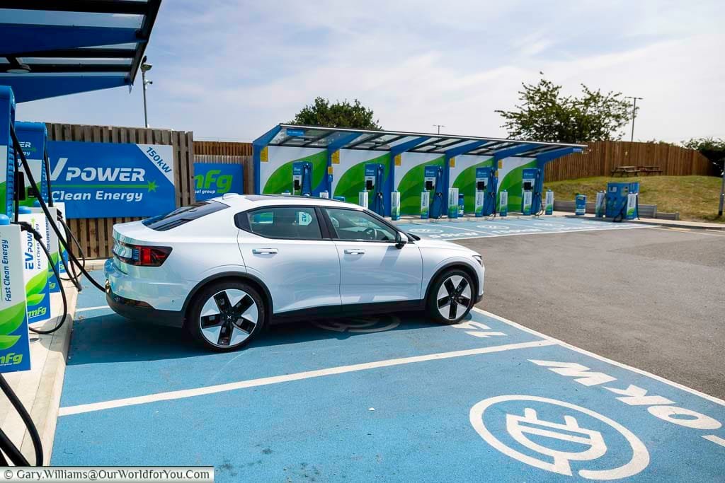A white Polestar 2 electric vehicle charges at a modern EV Power charging station in Newark, England, highlighting clean energy and fast-charging infrastructure. This image captures the convenience and sustainability of EV road trips across the UK, perfect for eco-conscious travel planning.