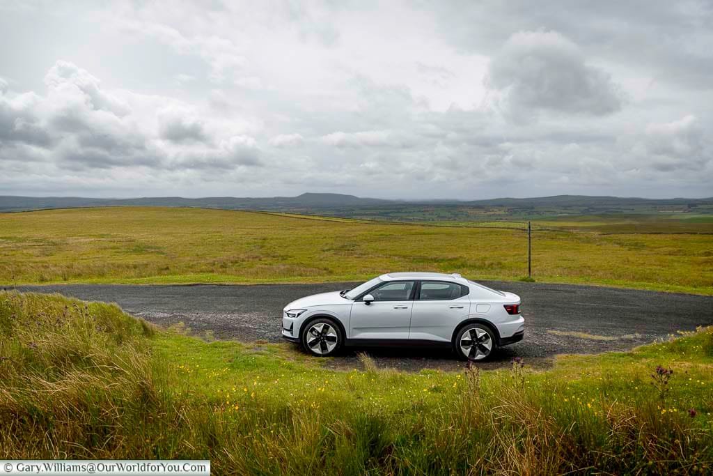 A white Polestar 2 electric car is parked on a quiet roadside in the heart of the Yorkshire Dales, surrounded by rolling green hills and a dramatic cloudy sky. This scenic shot captures the essence of sustainable travel through one of England’s most breathtaking national landscapes.